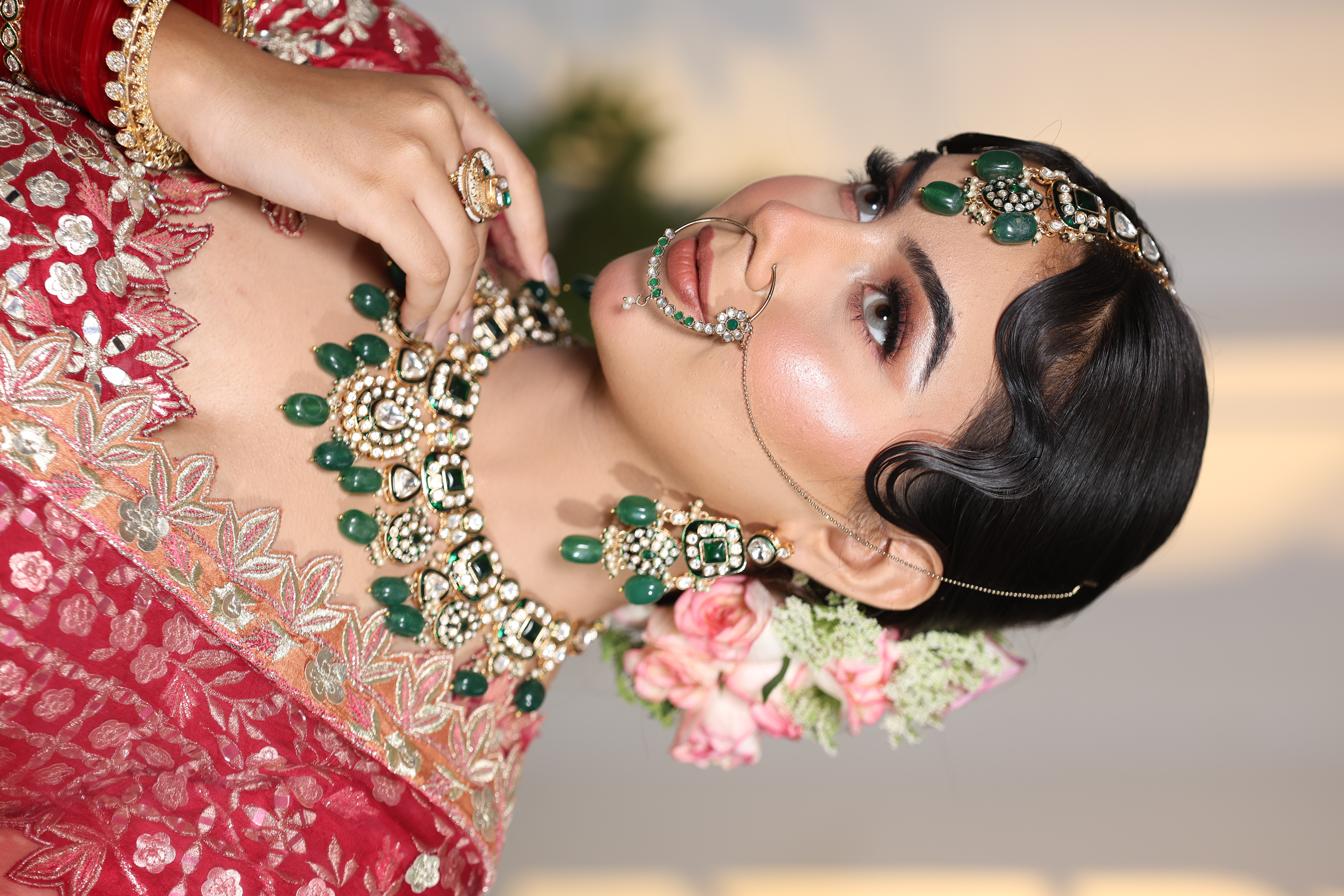 Close-up of bridal face showing retro finger waves, emerald kundan jewelry and glass skin finish